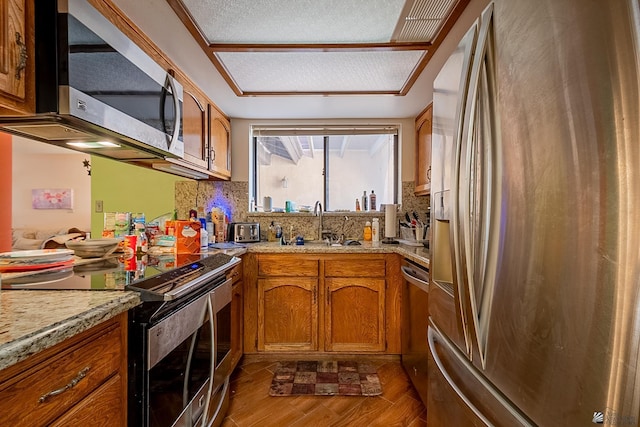 kitchen featuring tasteful backsplash, dark wood-type flooring, brown cabinets, stainless steel appliances, and a sink