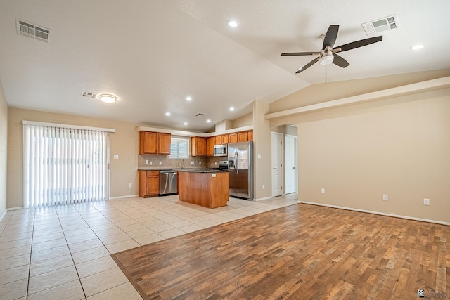 kitchen featuring ceiling fan, tasteful backsplash, lofted ceiling, a kitchen island, and appliances with stainless steel finishes