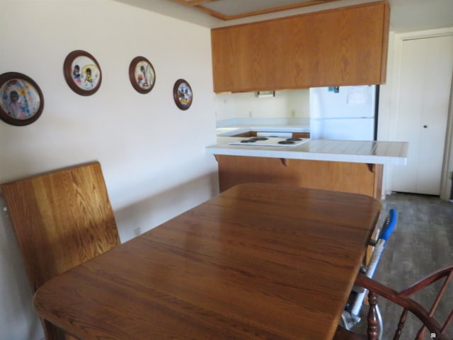 kitchen featuring white appliances, a peninsula, a breakfast bar area, brown cabinetry, and tile counters