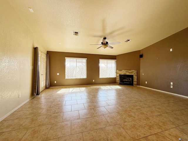 unfurnished living room featuring ceiling fan, light tile patterned flooring, a fireplace, and a textured ceiling