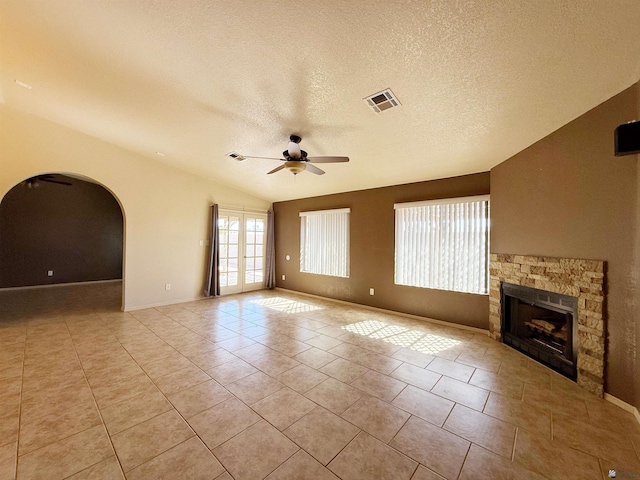 unfurnished living room with vaulted ceiling, light tile patterned flooring, a fireplace, ceiling fan, and a textured ceiling