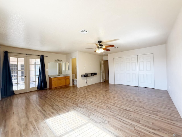 unfurnished living room featuring french doors, sink, ceiling fan, a textured ceiling, and light hardwood / wood-style flooring