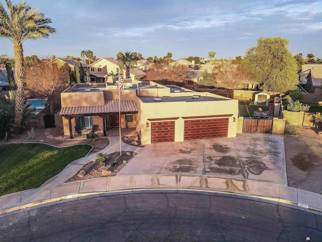 pueblo revival-style home featuring a front lawn, fence, stucco siding, driveway, and an attached garage