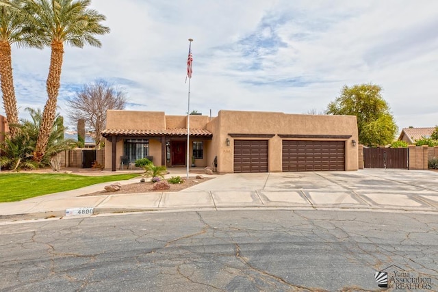 pueblo-style home with fence, a garage, driveway, and stucco siding