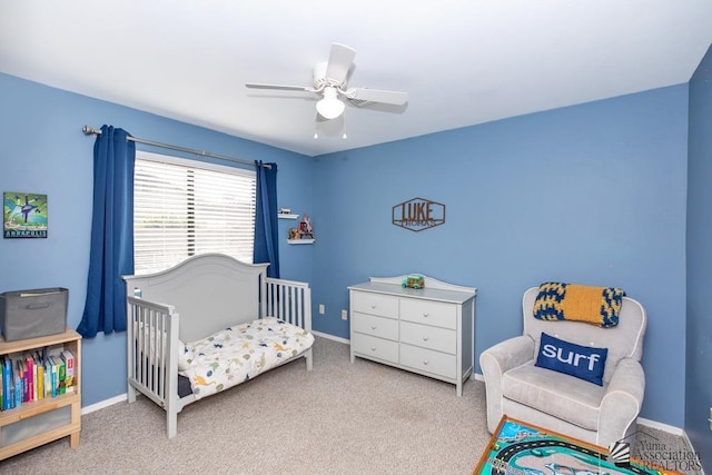 carpeted bedroom featuring a nursery area, baseboards, and ceiling fan