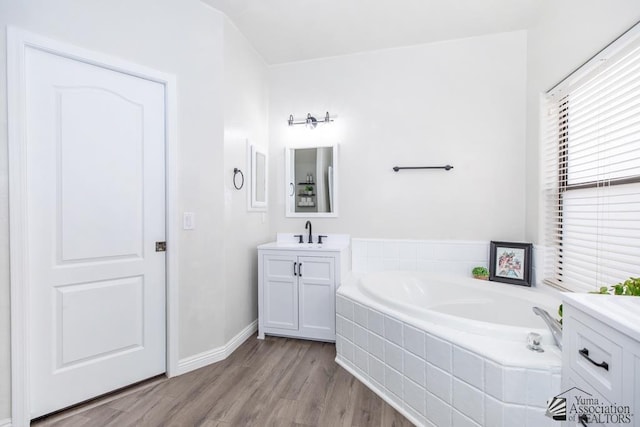 full bath with a bath, vanity, baseboards, and wood finished floors