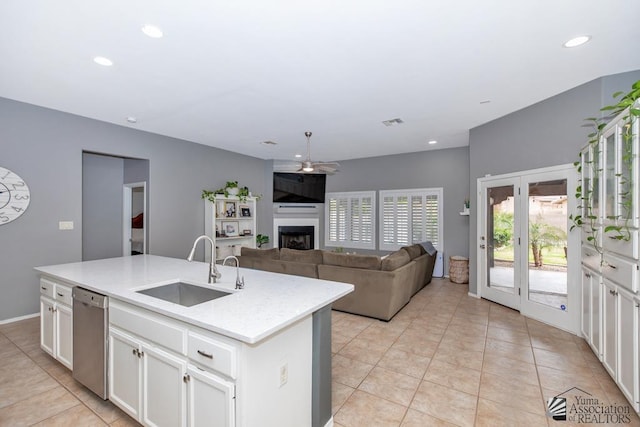 kitchen with a center island with sink, dishwasher, a fireplace, white cabinets, and a sink