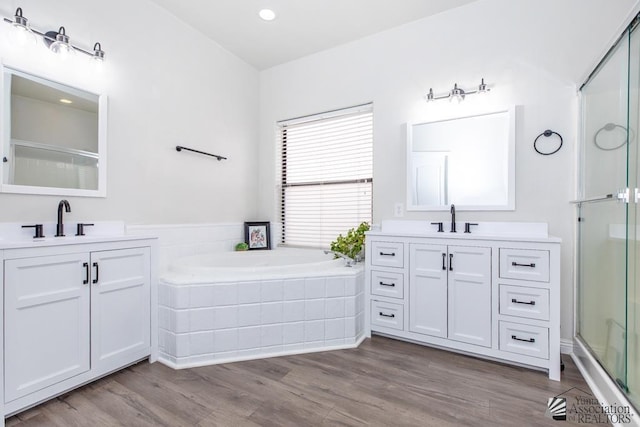 bathroom featuring wood finished floors, two vanities, a sink, a shower stall, and a garden tub