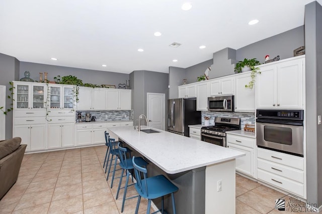 kitchen featuring light tile patterned floors, white cabinetry, a sink, stainless steel appliances, and a kitchen bar