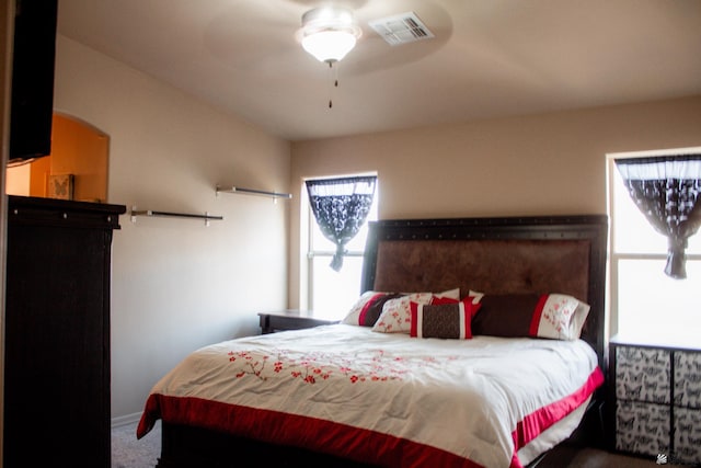 carpeted bedroom with visible vents, arched walkways, and a ceiling fan