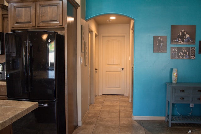 kitchen with light tile patterned floors, baseboards, arched walkways, and freestanding refrigerator