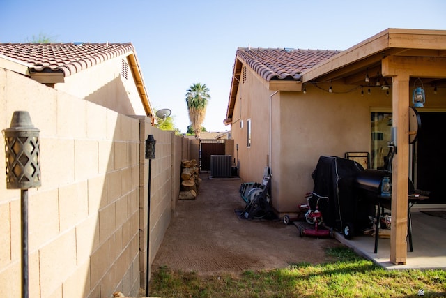 view of property exterior featuring a tile roof, cooling unit, fence, and stucco siding