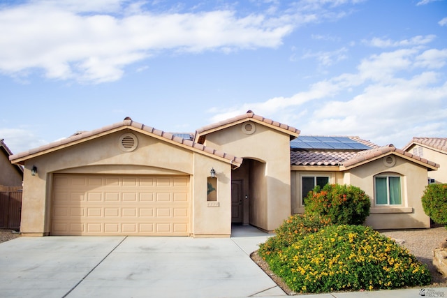 mediterranean / spanish-style house with concrete driveway, a tile roof, roof mounted solar panels, stucco siding, and a garage