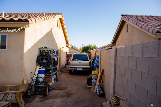 view of property exterior with a tiled roof, stucco siding, and fence