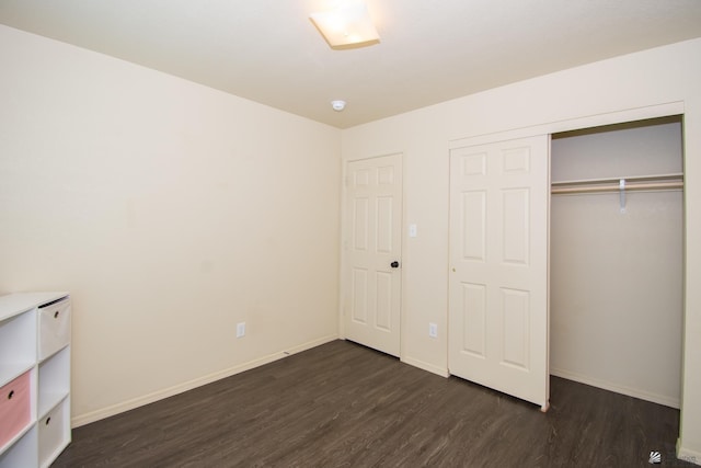 unfurnished bedroom with a closet, dark wood-style flooring, and baseboards