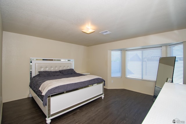 bedroom with a textured ceiling, wood finished floors, visible vents, and baseboards