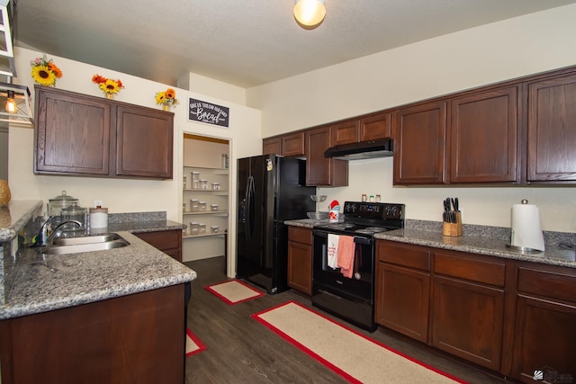 kitchen featuring stone countertops, dark wood-style floors, under cabinet range hood, black appliances, and a sink