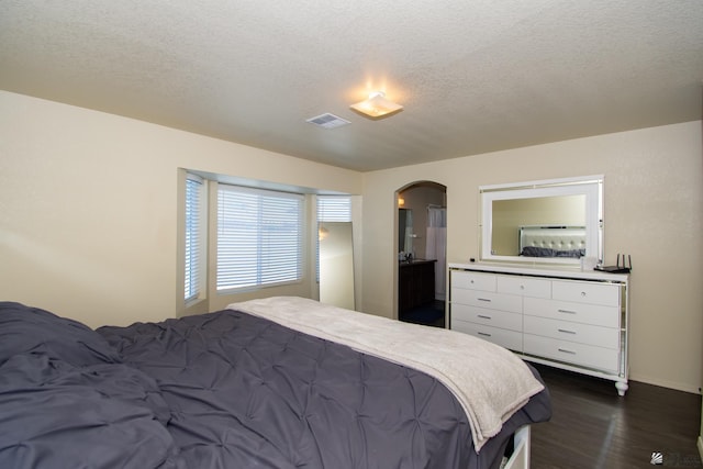 bedroom with dark wood-style floors, arched walkways, visible vents, and a textured ceiling