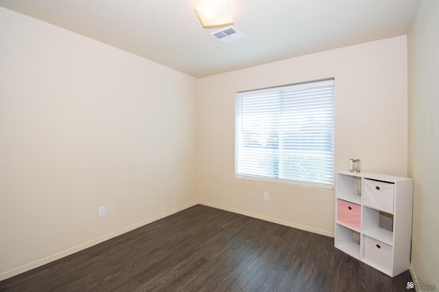 spare room featuring dark wood-style flooring, visible vents, and baseboards