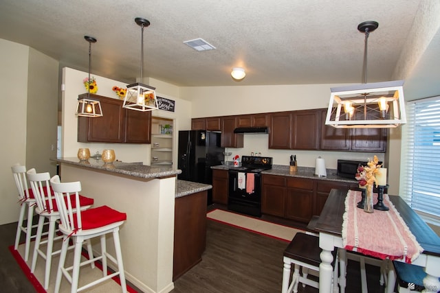 kitchen with a breakfast bar area, under cabinet range hood, dark wood-style flooring, visible vents, and black appliances