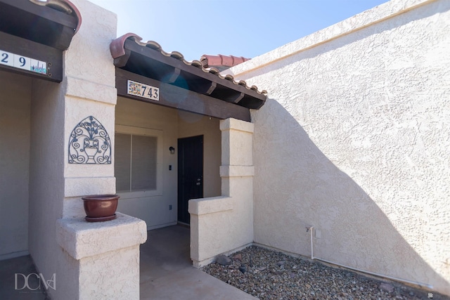 view of exterior entry with a tiled roof and stucco siding