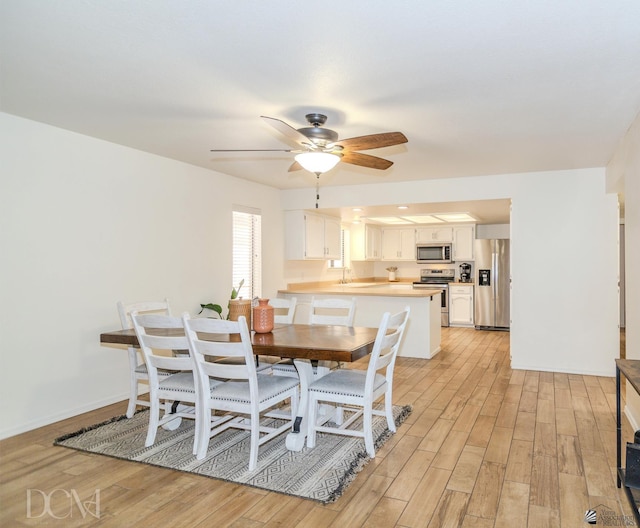 dining space featuring a ceiling fan, light wood-type flooring, and baseboards