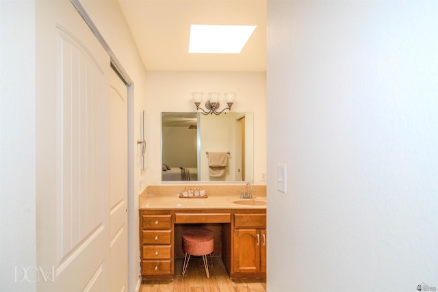 ensuite bathroom featuring a skylight, connected bathroom, wood finished floors, and vanity