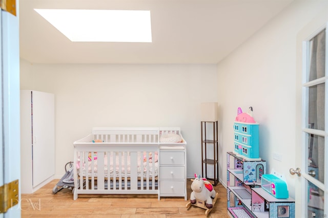 bedroom with a crib, a skylight, and wood finished floors