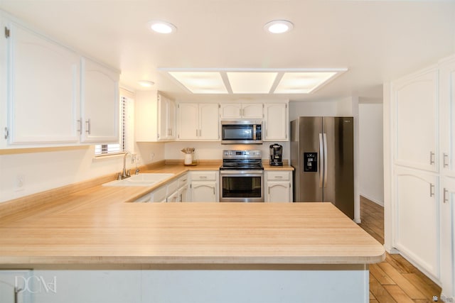 kitchen with appliances with stainless steel finishes, light countertops, a sink, and a peninsula