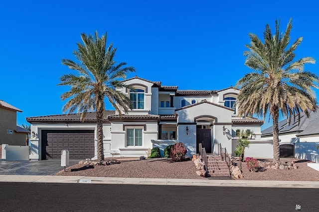 mediterranean / spanish-style house with a garage, driveway, a tiled roof, and stucco siding