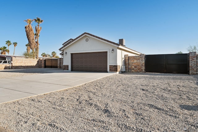 view of side of property with fence, concrete driveway, an attached garage, and a gate