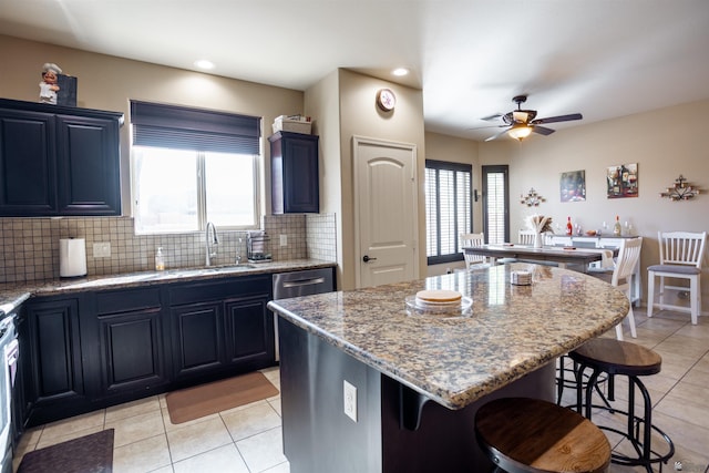 kitchen with a breakfast bar area, a kitchen island, a sink, ceiling fan, and backsplash