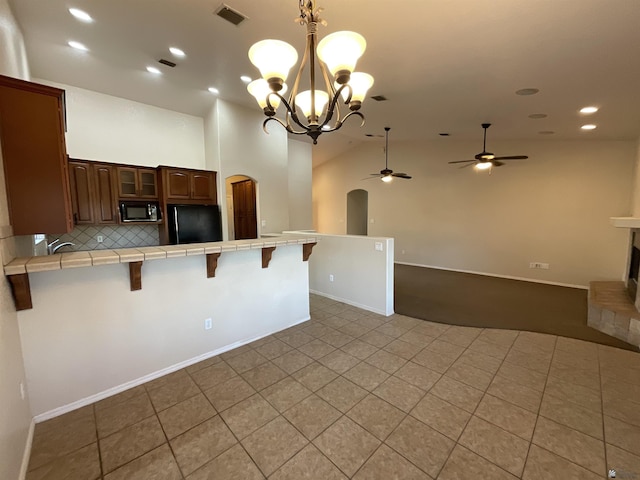 kitchen featuring a kitchen breakfast bar, tile counters, black appliances, tasteful backsplash, and ceiling fan with notable chandelier