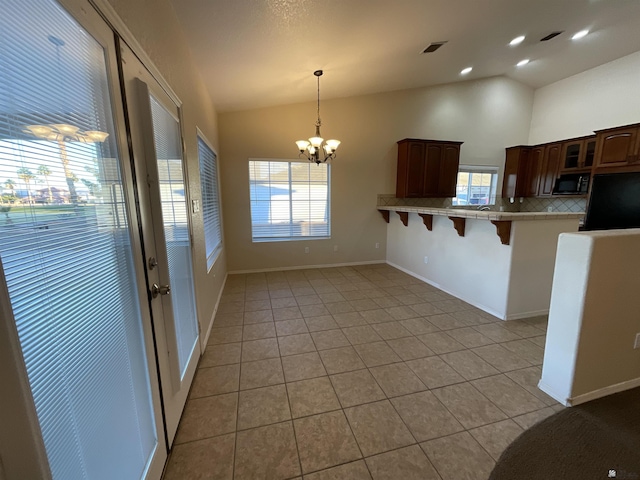 kitchen featuring vaulted ceiling, light tile patterned floors, kitchen peninsula, a breakfast bar area, and decorative backsplash