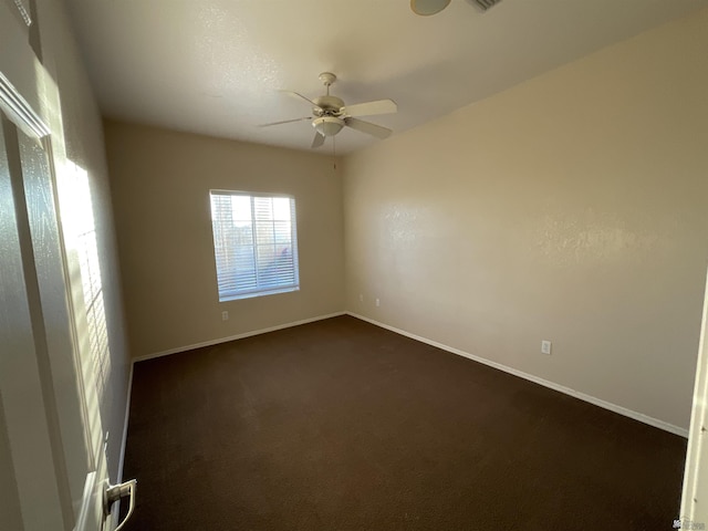 spare room featuring dark colored carpet and ceiling fan