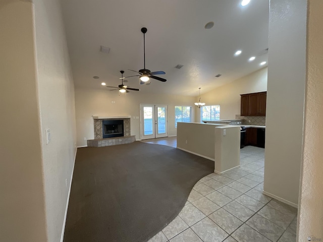 unfurnished living room with vaulted ceiling, french doors, a tiled fireplace, light tile patterned flooring, and ceiling fan with notable chandelier