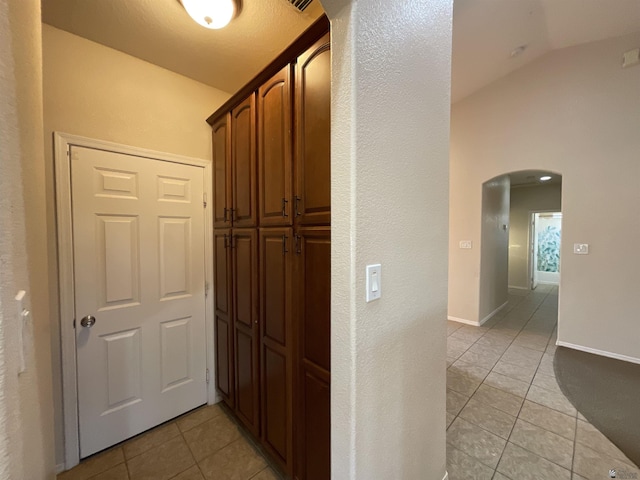 hallway featuring vaulted ceiling and light tile patterned flooring