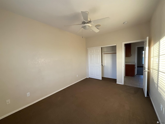 unfurnished bedroom with a closet, ceiling fan, and dark carpet