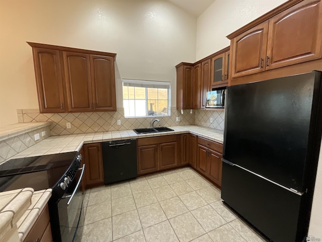 kitchen with tile counters, black appliances, a towering ceiling, decorative backsplash, and sink