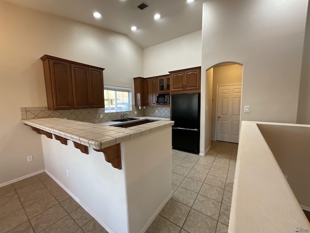 kitchen with kitchen peninsula, tile counters, decorative backsplash, high vaulted ceiling, and black appliances