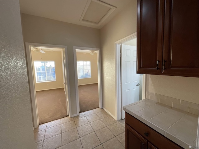 kitchen with ceiling fan, light carpet, tile countertops, and dark brown cabinets