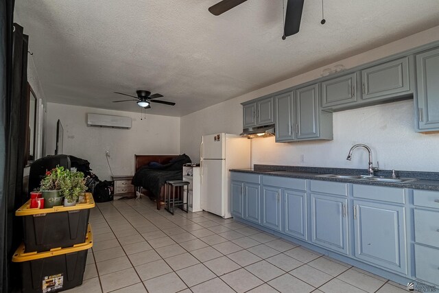 kitchen featuring white refrigerator, sink, light tile patterned floors, a textured ceiling, and a wall unit AC