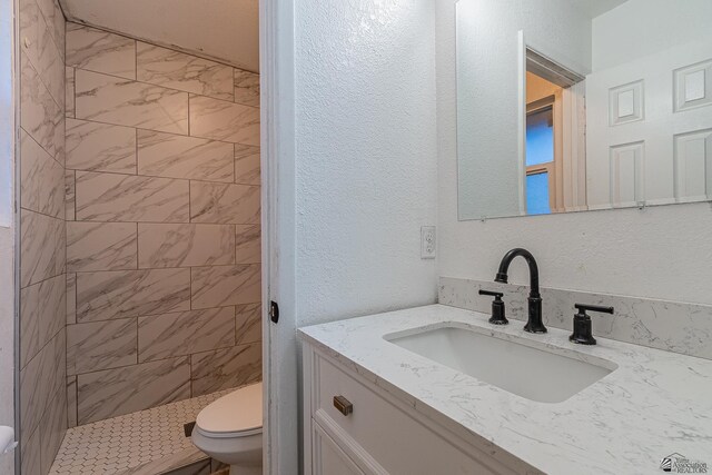 bathroom with toilet, vanity, and tiled shower