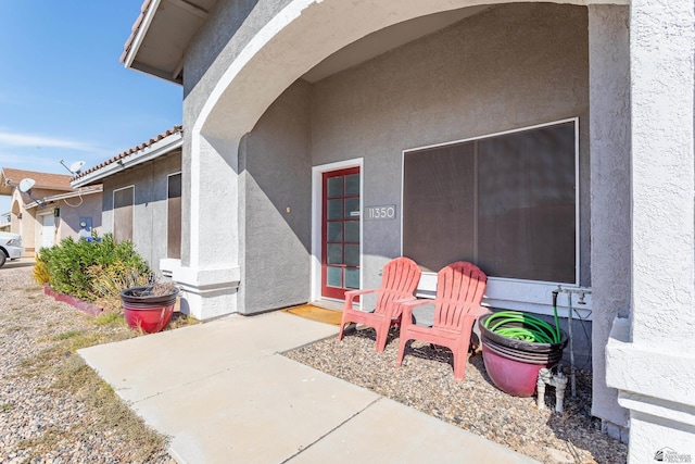 entrance to property featuring a tile roof, a patio area, and stucco siding