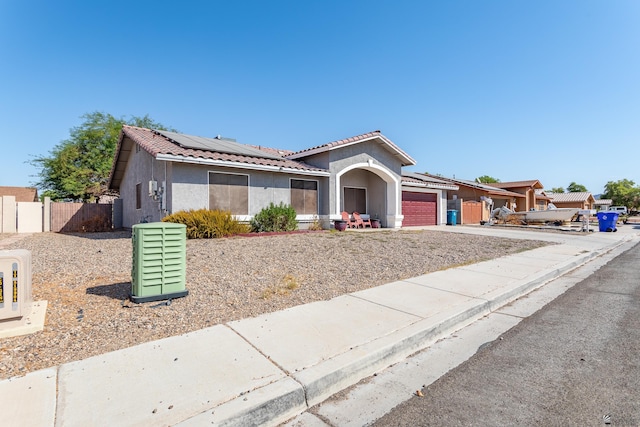 view of front facade with fence, solar panels, stucco siding, a garage, and a tile roof