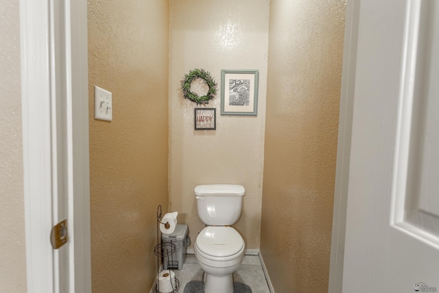 bathroom with tile patterned floors, toilet, baseboards, and a textured wall