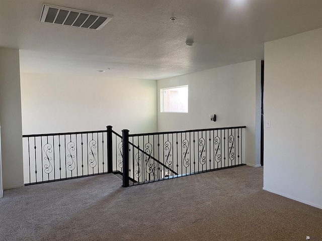 spare room with carpet floors, visible vents, a textured ceiling, and baseboards