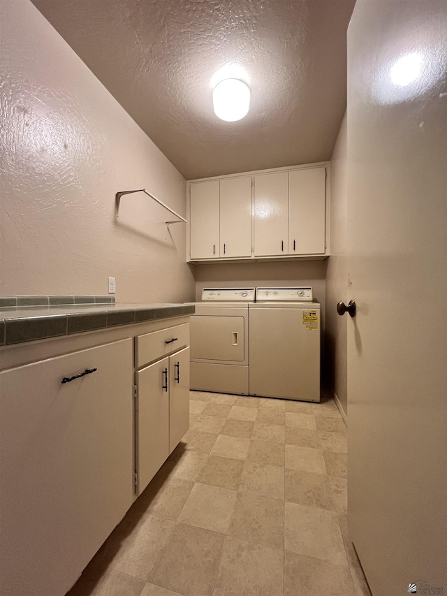 washroom featuring cabinets, a textured ceiling, and washing machine and clothes dryer