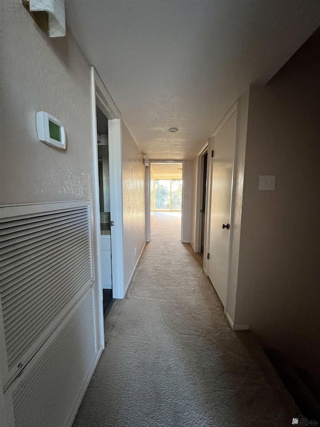 corridor with light carpet and a textured ceiling