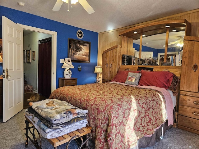 carpeted bedroom with a textured ceiling, ceiling fan, and wood walls